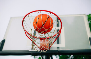 A close-up of a basketball going through a red hoop, framed against a clear sky and a blurred backboard. The action shot captures the moment of success, perfect for sports or achievement themes.