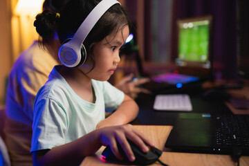 Asian young girl is playing a video game with a computer mouse. She is wearing headphones and she is focused on the game