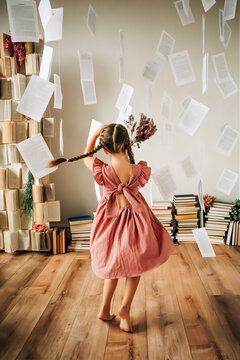 Girl with braids in a pink dress twirling in with floating pages