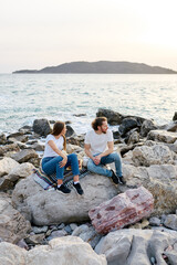 Two People Sitting on Rocks by Ocean