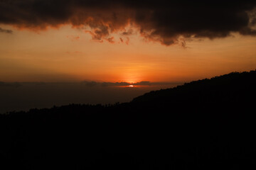 Sunset behind clouds and silhouetted hills