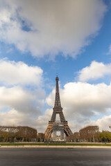 Fototapeta premium The Eiffel Tower stands tall and majestically under a beautifully dramatic sky in Paris, surrounded by lush green gardens and vibrant, lively scenery that captivates every visitor