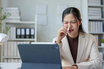 Asian woman stressed or tired, has a headache, is dizzy, sits and smells inhaler while working on a laptop. Asian business woman feeling sick at work, office syndrome concept.
