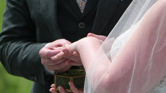 Groom places wedding ring on bride's finger during outdoor ceremony