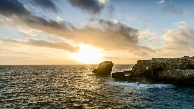 A sunset over the water and rocky coast of the seaside village of Binibeca. Time lapse.