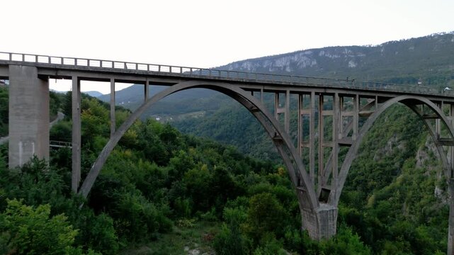 Flying underneath and through the Durdevica Tara Bridge turning around to reveal the whole bridge in the dusk evening in Montenegro europe sourrounded by forrest and mountains