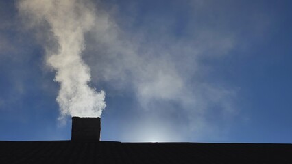 Silhouette of smoke against the sun from the chimney of a village house.