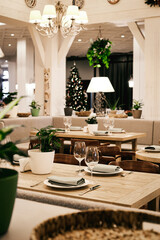 Christmas light modern interior of the restaurant with greenery with pleasant cozy lighting and festive table setting with glasses.