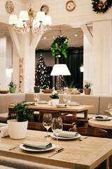 Christmas light modern interior of the restaurant with greenery with pleasant cozy lighting and festive table setting with glasses.