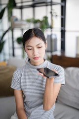 Asian woman using voice assistant on smartphone at home conversation with online assistant Voice chat bot conversational AI Modern Technologies.