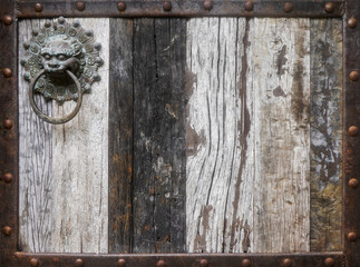 Ancient wooden gates in the castle with elements of antique door knocker pull handles  in the shape of a lion's head adorn the old wood colonial doors, close up