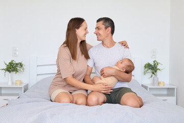 Family life warmth. Intimate parent-child hug. Mother and father hugging baby in cozy bedroom enjoying family bonding together parents cuddling child relaxing in bed