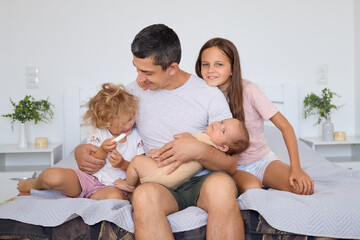 Father with infant and girls kids peacefully cradling baby relaxing in bright comfortable bedroom older sisters meeting newborn brother at home with love and tenderness