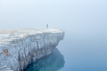 Man is standing on a cliff overlooking a foggy sea