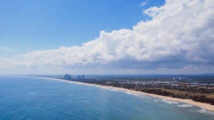 Aerial view of a tranquil, empty beach extending towards a cityscape, perfect for summer vacation or coastal nature concept