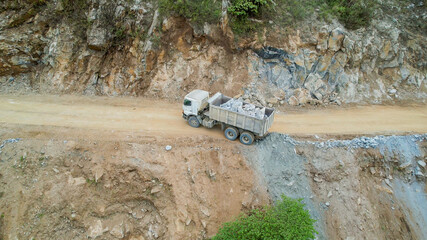 A truck transports rocks along a narrow dirt road in a quarry, highlighting industrial work and environmental impact