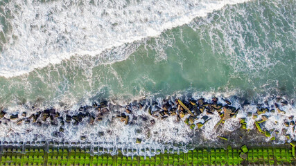 Aerial view of ocean waves crashing on a rocky shoreline, symbolizing coastal erosion and...