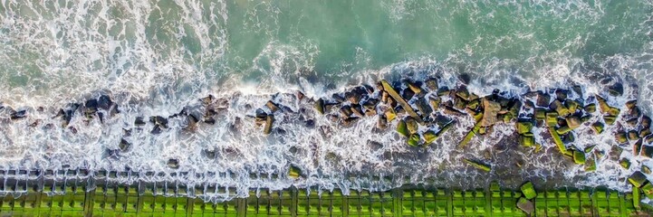 Aerial view of the ocean waves crashing against a mossy rocky shoreline, symbolizing erosion and...