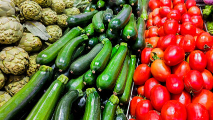 Fresh zucchini, tomatoes, and artichokes at a market, highlighting healthy eating and organic produce