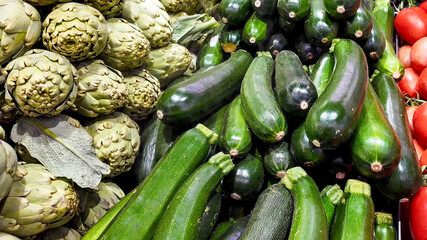 Fresh organic artichokes, zucchinis, and tomatoes at a farmer's market, promoting healthy eating and local agriculture sustainability
