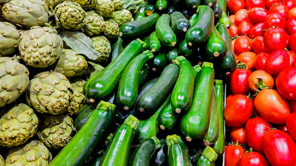 Fresh organic produce including artichokes, zucchini, and tomatoes on display at a farmers' market, promoting healthy eating and sustainability