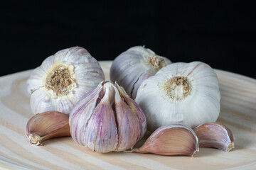 Fresh purple garlic heads and cloves on a rustic wooden plate with black background.