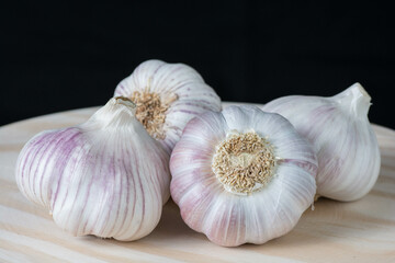 Fresh purple garlic heads and cloves on a rustic wooden plate with black background.