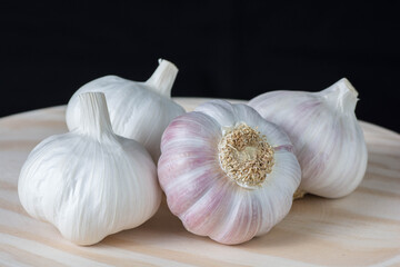 Fresh pink garlic heads and cloves on a rustic wooden plate with black background.