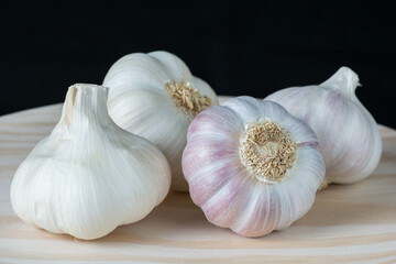 Fresh pink garlic heads and cloves on a rustic wooden plate with black background.