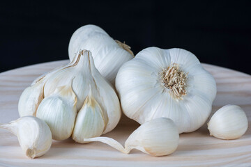 Fresh garlic heads and cloves on a rustic wooden plate with black background.
