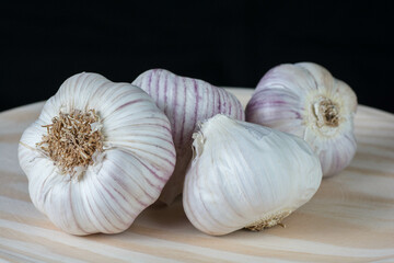 Fresh purple garlic heads and cloves on a rustic wooden plate with black background.