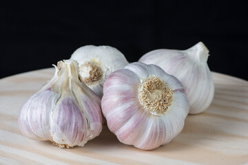 Fresh pink garlic heads and cloves on a rustic wooden plate with black background.