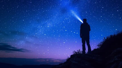 Fototapeta premium A lone figure stands on a rocky cliff, illuminating the star-filled sky with a flashlight. The serene night scene evokes feelings of solitude, wonder, and the beauty of nature.
