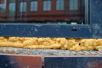 Yellow polyurethane foam sealant filling the seams around  newly installed window,  ensuring...