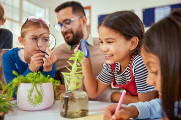 Cute little girl observing plants during biology lesson at primary school