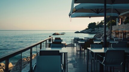 An empty seaside terrace with minimalist furniture overlooks the calm ocean, evoking a sense of solitude and peaceful contemplation at dawn.