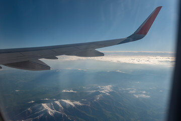 Obraz premium Wing of an airplane flying above the clouds in the blue sky.