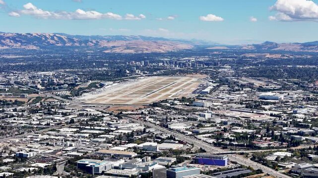 Aerial view of San Jose International Airport with surrounding urban landscape and distant mountain ranges under a clear sky in Silicon Valley, California.
