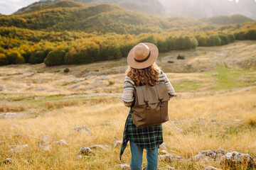 A woman stands on rocky terrain, gazing at the vibrant autumn trees and mountains. Eco tourism. Active lifestyle.