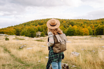 A woman stands on rocky terrain, gazing at the vibrant autumn trees and mountains. Eco tourism. Active lifestyle.