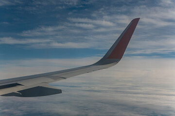 Obraz premium Wing of an airplane flying above the clouds in the blue sky.