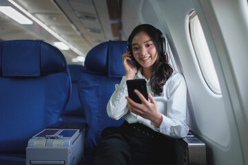 Confident Asian businesswoman sitting in business class luxury plane while wearing wireless headphones to relax Listen to music and work on your personal online business during international flights.