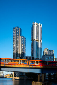A vibrant red train crosses an elevated track under a clear blue sky, with towering modern buildings in the background, capturing urban dynamism and connectivity.