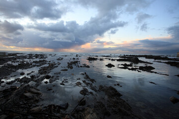 View of tranquil ocean waves and dramatic rocks under a serene sunset sky, Cape Town, South Africa.