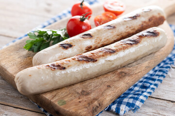 Grilled bratwurst sausages with tomatoes on wooden table