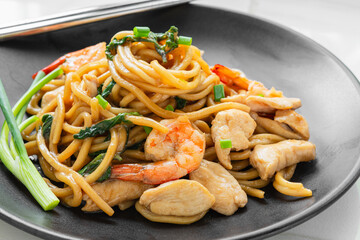 Delicious yakisoba noodles stir-fried with basil and dried chillies. Stir-fried with oyster sauce, soy sauce and chicken fillet, shrimp, decorated with scallions on a black plate. Home cook.