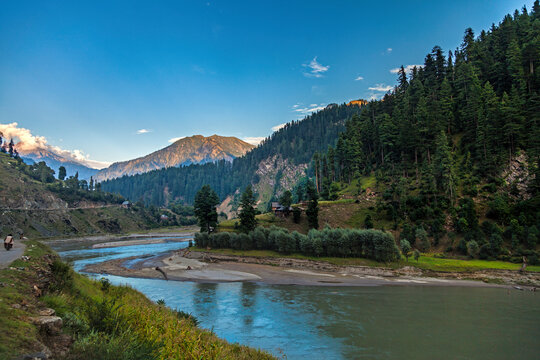 View of beautiful landscape with a serene river, majestic mountains, and lush forest, Kashmir, Pakistan.