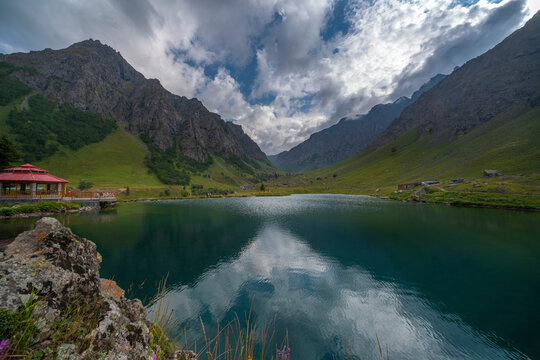 View of serene lake surrounded by majestic mountains and vibrant greenery under a beautiful sky with clouds, Minimarg, Pakistan.