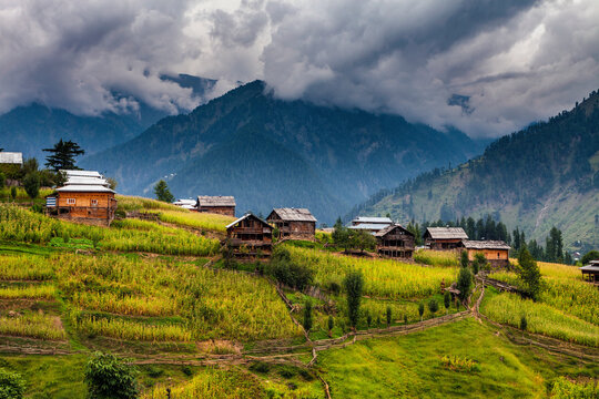 View of serene Neelum Valley with picturesque wooden houses and lush fields surrounded by majestic mountains, Kashmir, Pakistan.