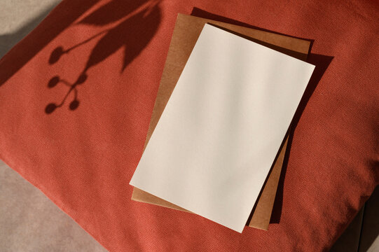 Autumn greeting postcard or wedding invitation design template, empty paper card texture mockup, brown envelope on terracotta red textured pillow with aesthetic floral sunlight shadows